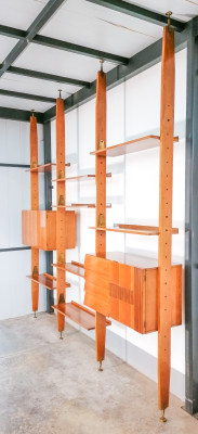 Wall Unit modulare con fissaggio a pavimento e soffitto. Il mobile è composto da 8 ripiani e due armadietti con ante, ripiani (di cui uno in vetro) e cassettini. Viene fissato al soffitto e al pavimento mediante piedini girevoli in ottone, per cui può essere collocato in qualsiasi posizione all
