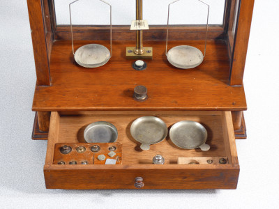Bilancia da farmacia di precisione, teca in legno, con meccanismo di sollevamento dei piatti, cassetto e pesini. Italia, Fine Ottocento Primo Novecento