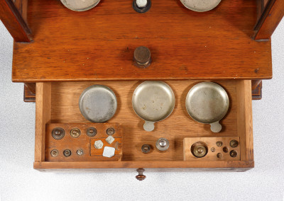 Bilancia da farmacia di precisione, teca in legno, con meccanismo di sollevamento dei piatti, cassetto e pesini. Italia, Fine Ottocento Primo Novecento
